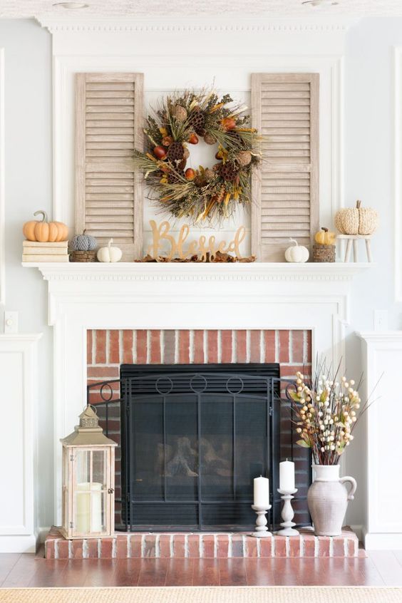 lovely rustic decor with a red brick fireplace, a vintage mantel, faux pumpkins, a lush grass and nut wreath and stained shutters