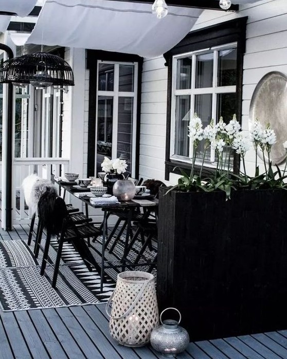 a laconic Scandinavian dining space with black furniture, a tall planter as a space divider, candle lanterns and pendant lamps