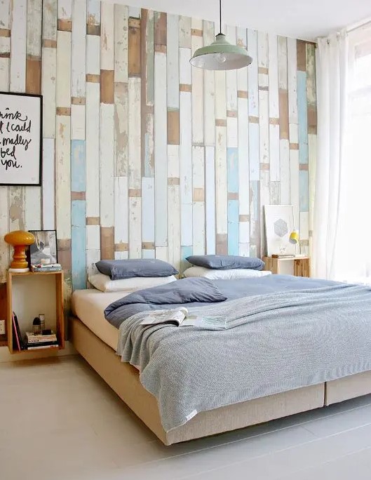 an accent wall done with various shabby wooden planks in white, beige and blue adds a nonchalant touch to the bedroom