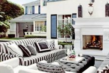 14 a lovely outdoor living room with a fireplace, striped black and white sofas, white chairs, a black upholstered ottoman and some greenery