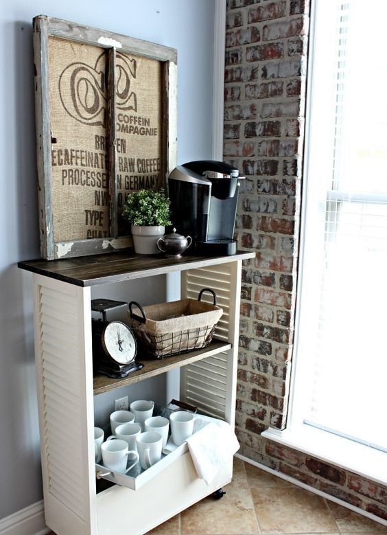 a cozy rustic drink station   a piece on casters made of shutters, a stained countertop, a rustic artwork, some mugs and a coffee machine