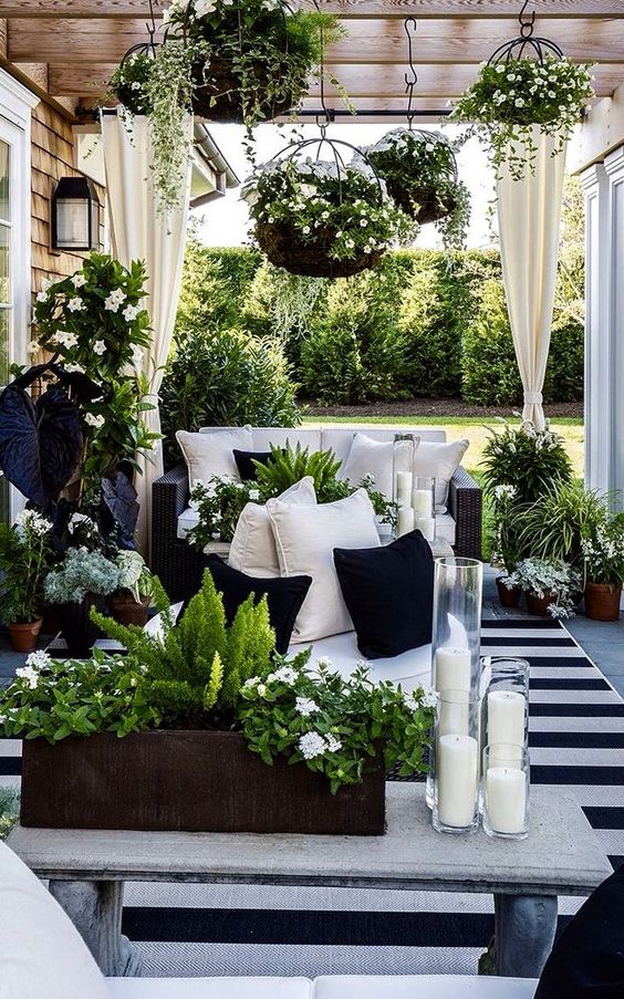 a monochromatic terrace with black wicker furniture, black and white pillows, potted greenery and white blooms and a striped rug