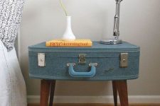 17 a stylish nightstand made of a blue fabric upholstered suitcase on legs, with a metal table lamp and a vase