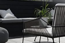 19 a Nordic terrace with a grey deck, a black built-in bench, a black chair with white upholstery and greenery