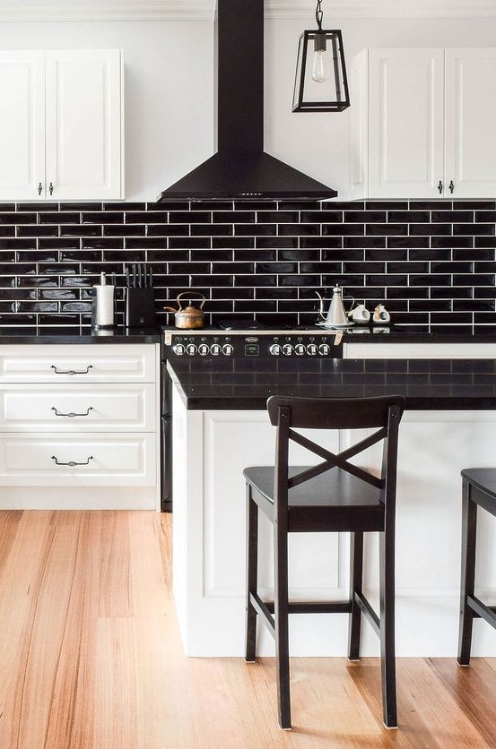 a white farmhouse kitchen with black glossy tiles, a black hood and countertops plus black stools