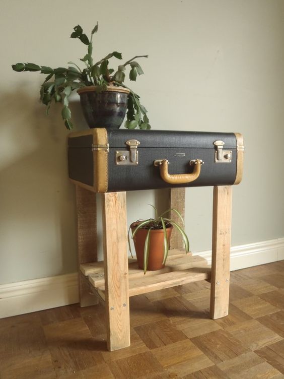 a black vintage suitcase placed on wooden legs, with a wooden shelf is a lovely console table and plant stand at the same time