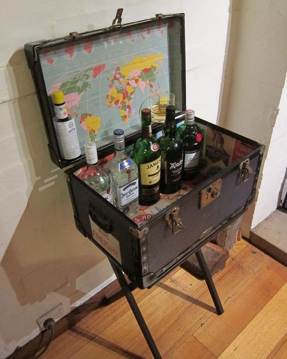 a black vintage suitcase placed on trestle legs, with new map lining inside and various bottles   a creative home bar