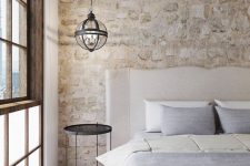 22 a chic serene bedroom with a stone accent wall, a neutral upholstered bed with neutral bedding, a sphere pendant lamp is cool