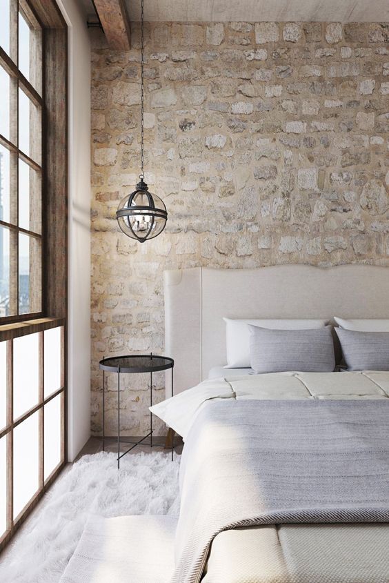 a chic serene bedroom with a stone accent wall, a neutral upholstered bed with neutral bedding, a sphere pendant lamp is cool
