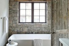 23 a faux stone wall and weathered wood on the floor make this bathroom cabin-like