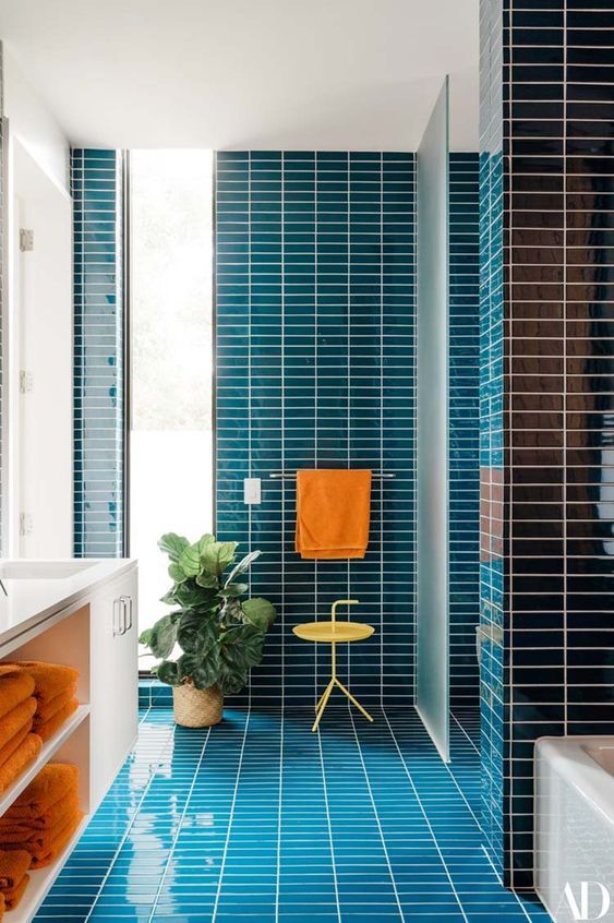 a bold bathroom clad with blue skinny tiles, with a floating white vanity and orange towels is an amazing space infused with color