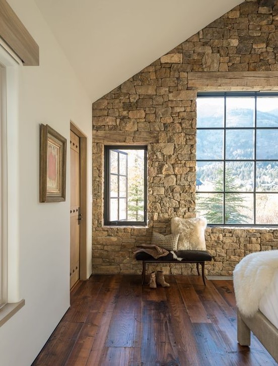 a cabin bedroom with a stone accent wall, an attic roof, modern furniture and a gorgeous mountain view is very welcoming