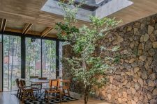 28 a dining space with a skylight, a tree under it and a stone accent wall to bring nature inside the house