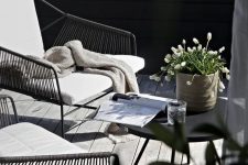 28 a small modern terrace with metal and wicker chairs, a black table, some simple blooms in a pot and a weathered deck