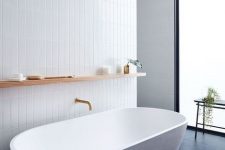 30 a chic minimalist bathroom with white skinny tiles on the wall and a white oval bathtub plus black tiles on the floor