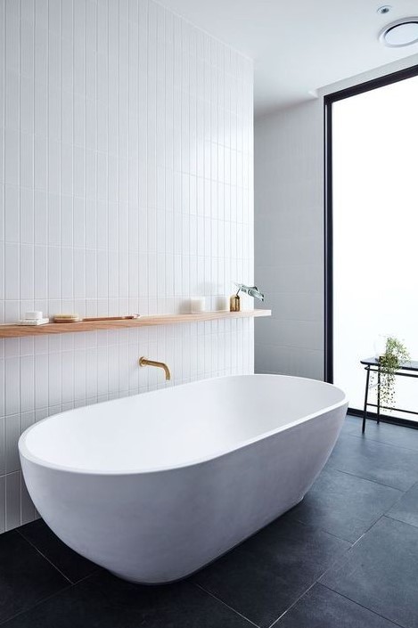 a chic minimalist bathroom with white skinny tiles on the wall and a white oval bathtub plus black tiles on the floor