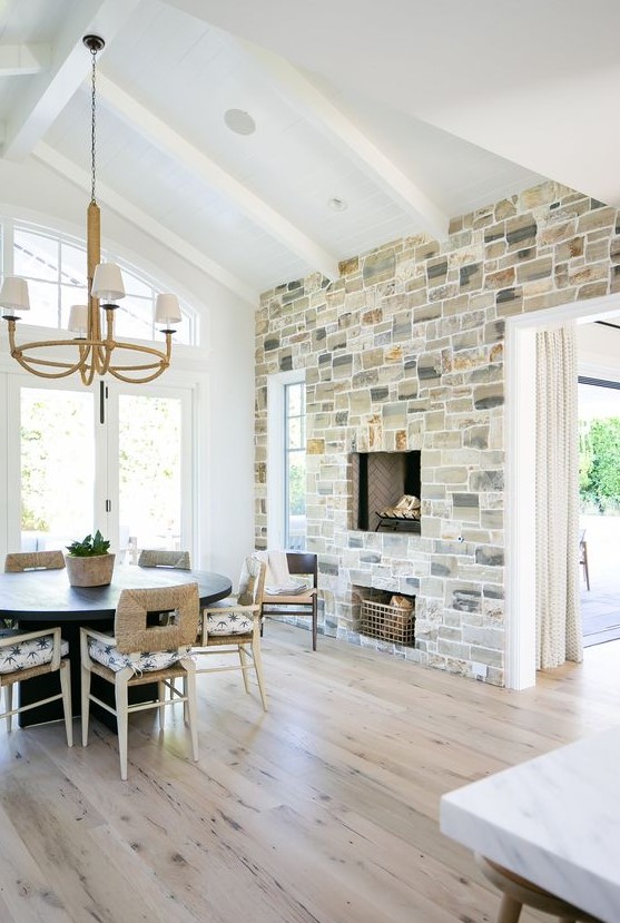 a modern farmhouse dining space with a stone accent wall with a fireplace, a black round table and catchy chairs