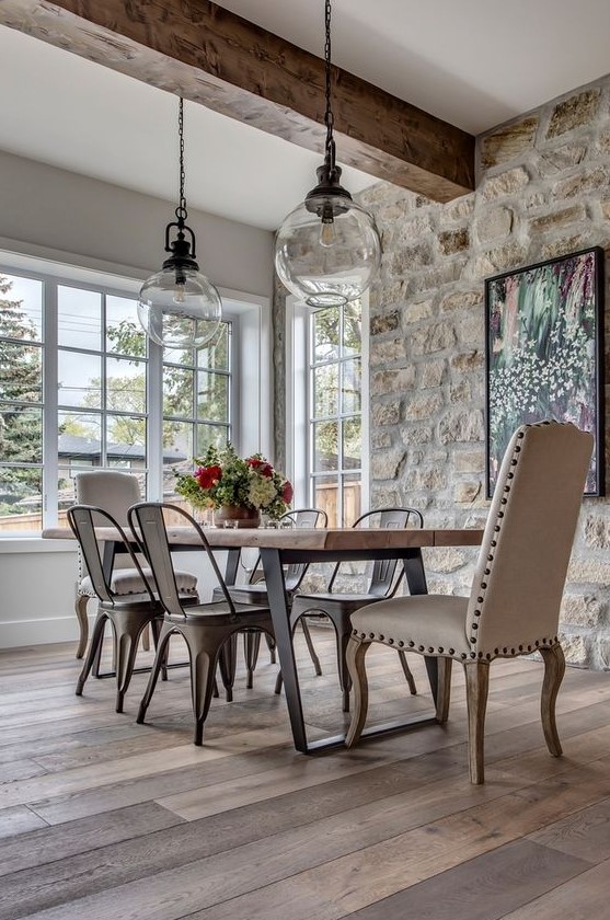 a modern French country kitchen with a stone accent wall, a wooden table and metal chairs and a leather chair plus pendant lamps