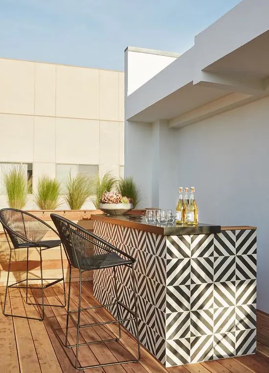 an outdoor bar with a tiled black and white bar countertop and black stools and potted greenery and lots of drinks