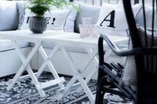 35 a black and white Scandinavian balcony with a printed rug, a white corner sofa, a black chair and white folding tables and greenery