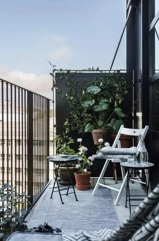 a black balcony done with a couple of folding chairs and a small coffee table plus a lot of greenery around