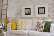 37 a bright living room with a whitewashed brick walls, a white sofa, colorful pillows, bamboo candles and bright accessories
