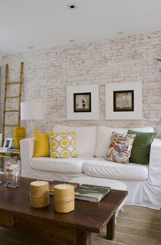 a bright living room with a whitewashed brick walls, a white sofa, colorful pillows, bamboo candles and bright accessories