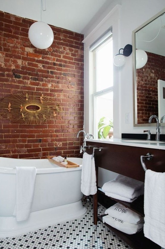 a chic bathroom done in white and with contrasting touches   a red brick wall and a rich toned vanity