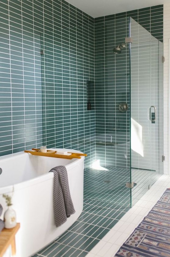 a mid century modern bathroom with teal skinny tiles, a white tub and a printed rug is a very welcoming space