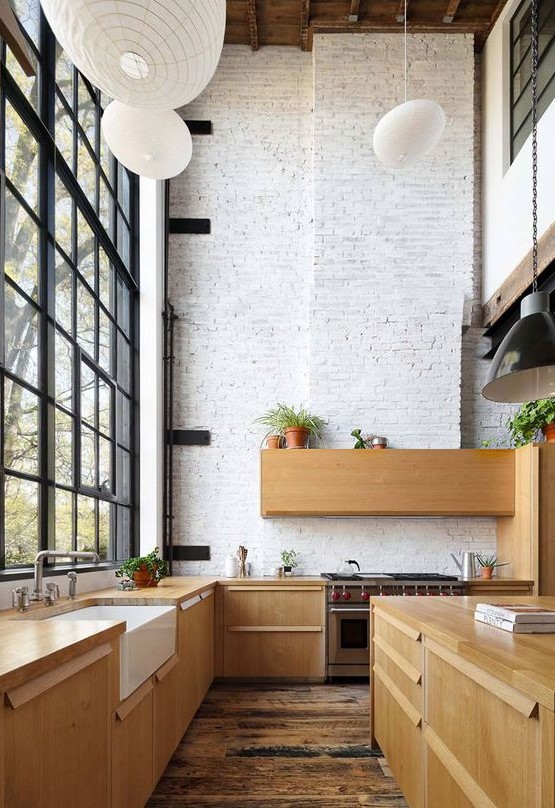 a modern double height kitchen with whitewashed brick walls, sleek wooden cabinetry, pendant lamps and potted greenery