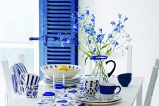 41 a lovely Greek-inspired dining space with a storage unit with a super bold blue shutter door, white dining furniture, blue and white tableware