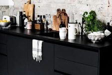 42 a Nordic kitchen with a whitewashed brick wall, black sleek cabinetry, black sconces and some herbs in pots is a very stylish space