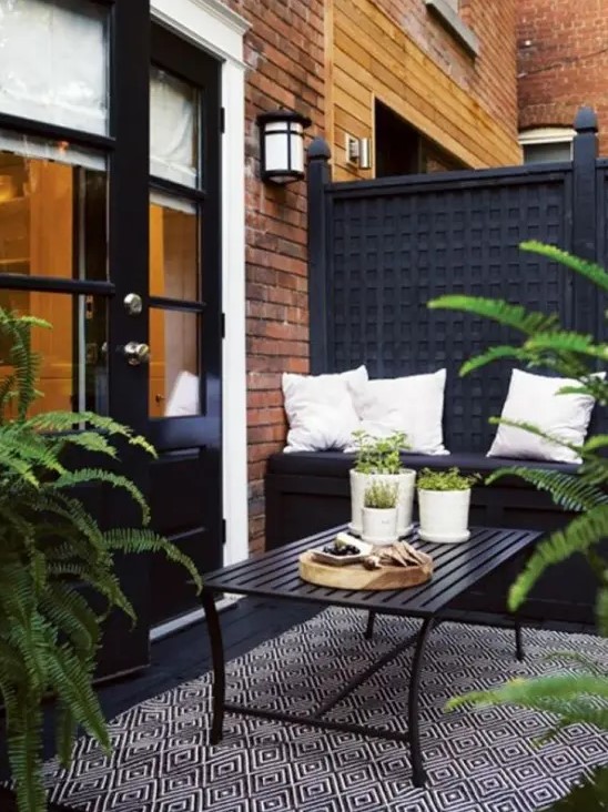 a Nordic balcony with a black wall, a black built-in bench and a wooden table, a printed chair and potted greenery to refresh the space
