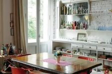 46 an eclectic dining space with a whitewashed bricl wall, a large buffet and shelves, a refined wooden table and modern red chairs