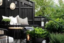 47 a Scandinavian balcony with black walls, a black built-in bench, a neutral hairpin leg table, black chairs and black pots with greenery