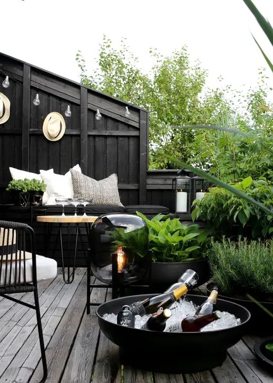 a Scandinavian balcony with black walls, a black built-in bench, a neutral hairpin leg table, black chairs and black pots with greenery