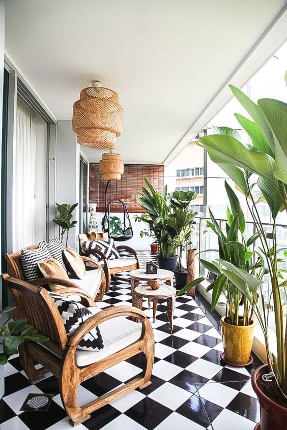a stylish black and white balcony with a checked tile floor, wooden chairs and a sofa with black and white upholstery, potted greenery and woven pendant lamps