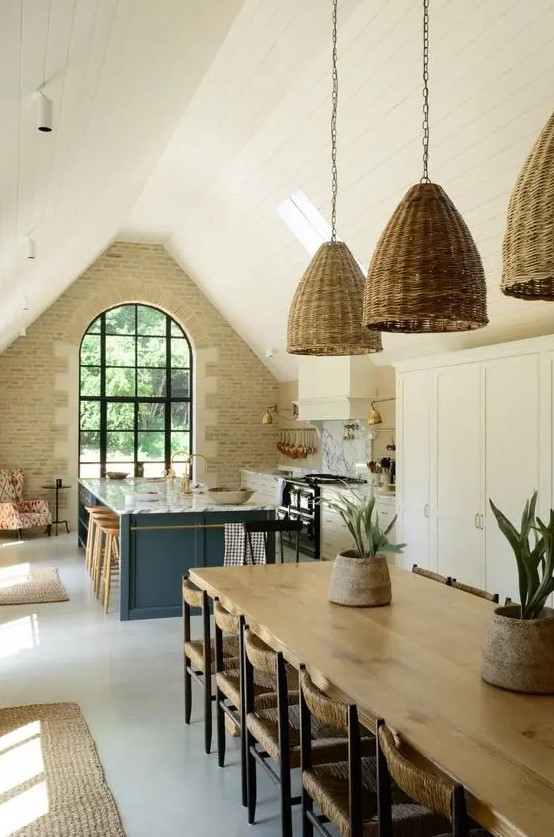 a barn kitchen with a stone accent wall, an arched window, white shaker style cabinets, a stone blue kitchen island and woven pendant lamps