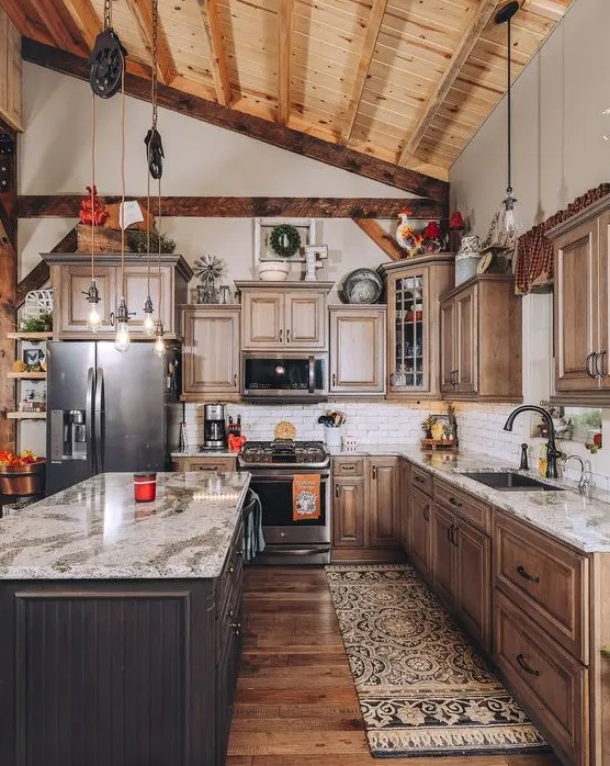 a barn kitchen with a wooden ceiling and wooden beams, stained shaker style cabinets, a dark stained kitchen island and stone countertops