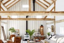 a barn living room clad with whitewashed planks, with leather chairs, a grey sofa, a vintage hearth, a tiered coffee table and greenery