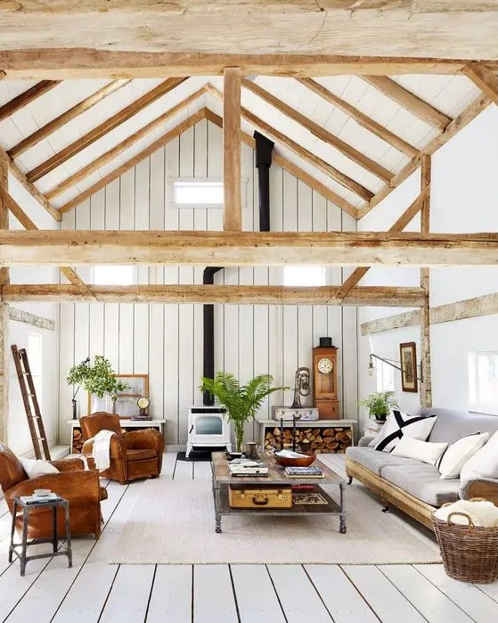 a barn living room clad with whitewashed planks, with leather chairs, a grey sofa, a vintage hearth, a tiered coffee table and greenery