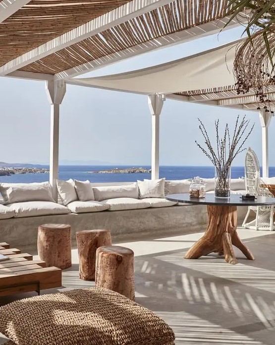 a beach patio with a concrete bench, neutral upholstery, wooden and woven furniture and accessoeies and a beautiful sea view