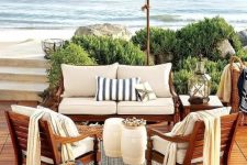 a beach patio with a deck, rich-stained wooden furniture with neutral upholstery, candle lanterns and corals and baskets