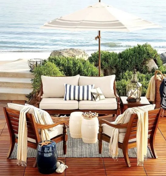 a beach patio with a deck, rich-stained wooden furniture with neutral upholstery, candle lanterns and corals and baskets