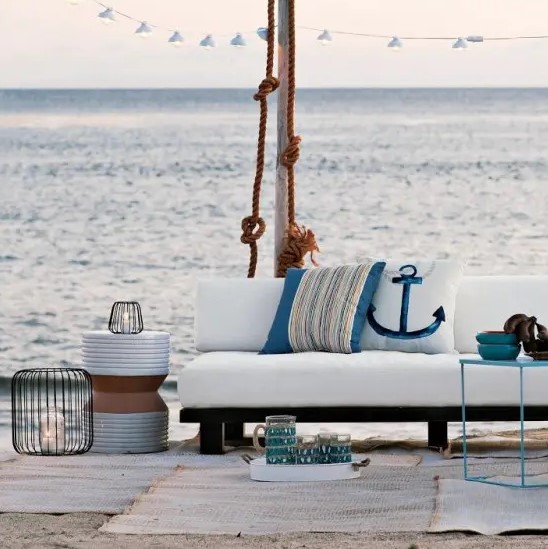 a beach patio with white upholstered furniture, neutral rugs, some rope, seaside pillows and candle lanterns