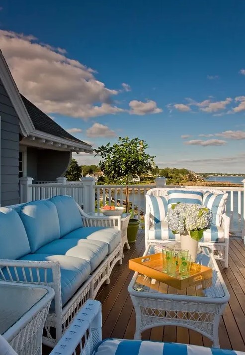 a beach porch with white wicker furniture, blue upholstery, potted plants and blooms and a beautiful sea view