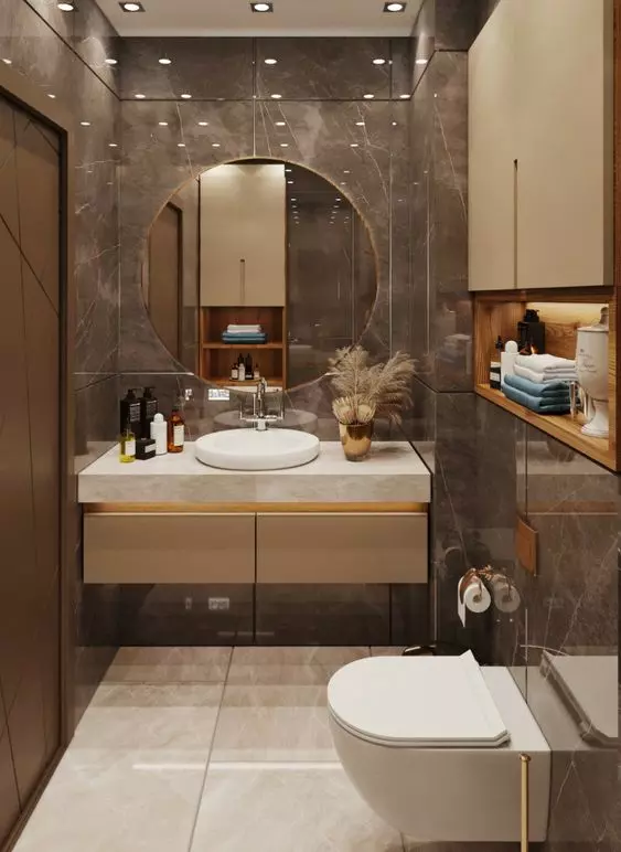 a beautiful and exquisite bathroom clad with brown marble tiles and white ones, a built in vanity with a round sink and a round mirror