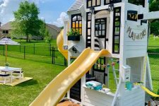 a beautiful black and white kids’ playhouse with black window frames, with a small space inside, a yellow slide and another one on the other wall