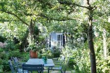 a beautiful garden dining zone with blue furniture and greenery and blooms plus trees around is chic