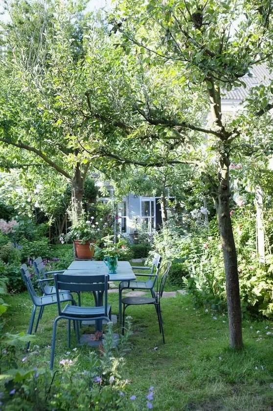 a beautiful garden dining zone with blue furniture and greenery and blooms plus trees around is chic